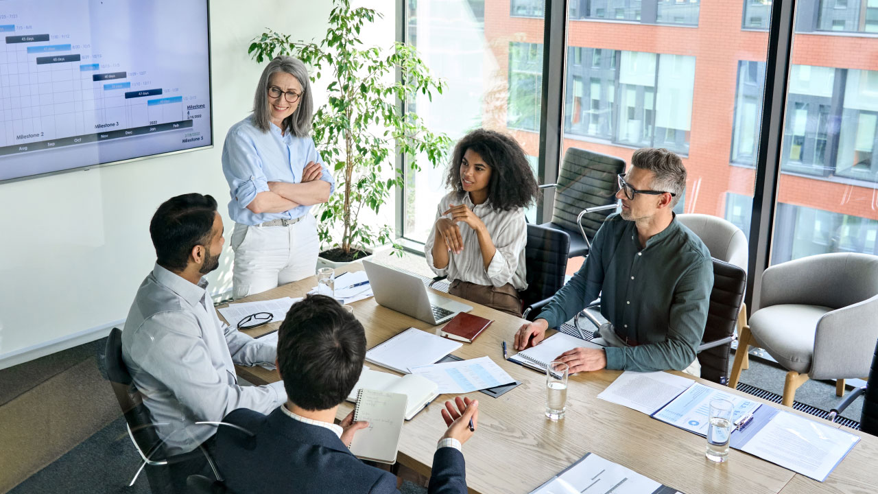 A group of professionals surround a table and watch a business presenation