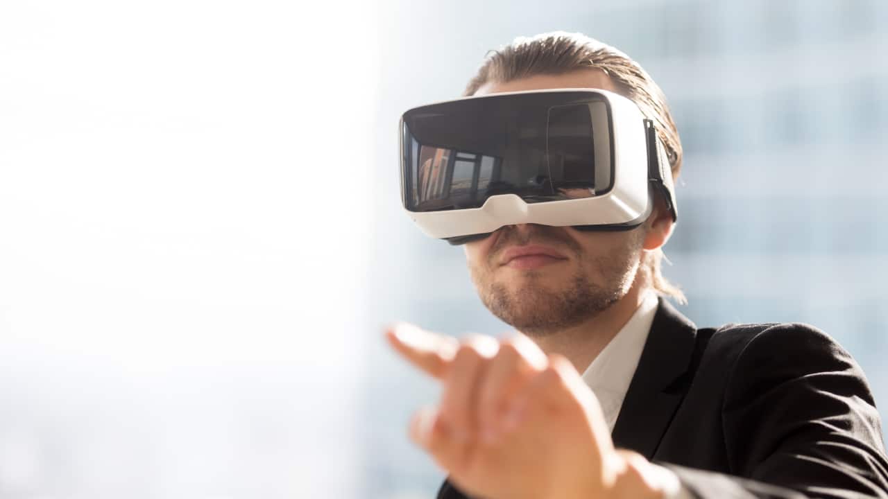 A well-dressed man wears a virtual reality headset and points to something he sees.