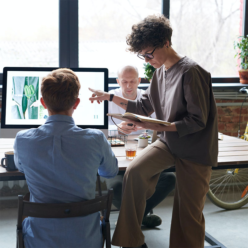 woman sitting on desk pointing at computer